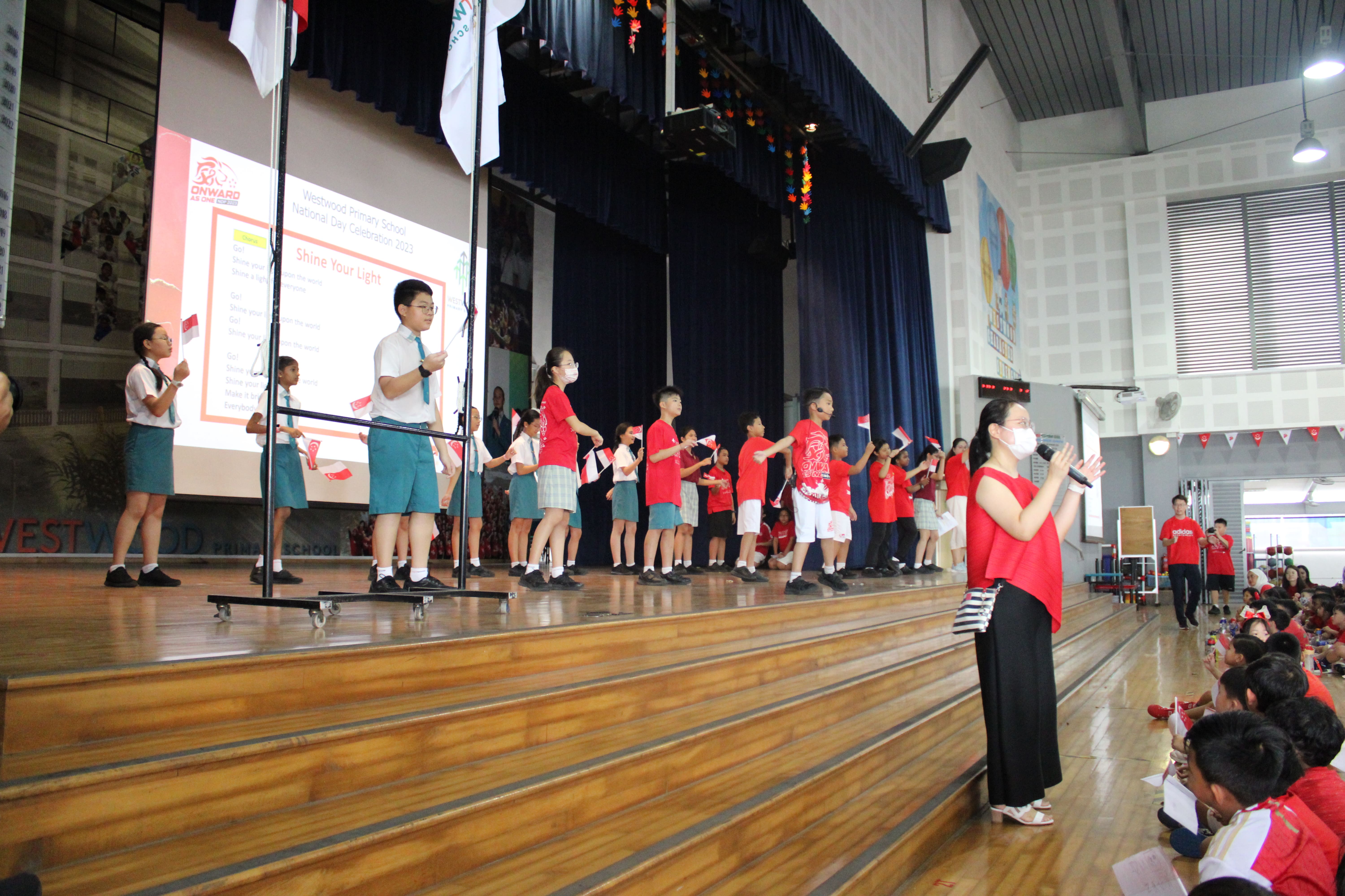 Students in red and school uniforms perform on a stage during Westwood Primary School National Day Celebration 2023.